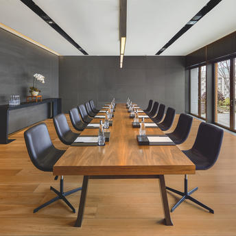 Boardroom at Amanyangyun with long wooden table and black chairs, grey walls and natural light from windows.