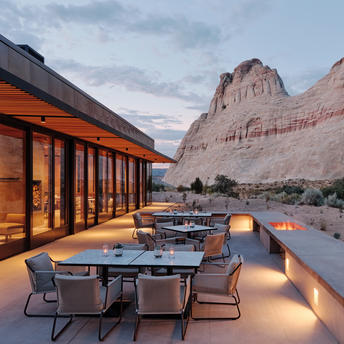 Dining terrace at dusk with tables set beneath a towering sandstone cliff at Amangiri resort.