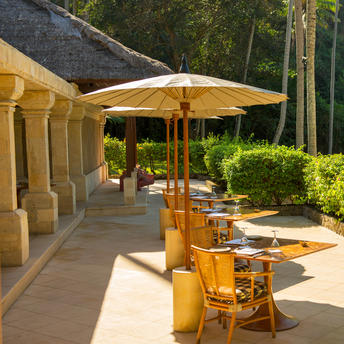 Wooden deck at Amankila with yellow umbrellas and dining chairs overlooking landscaped gardens.