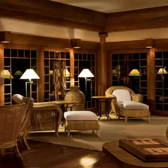 Amanpulo resort library with warm wooden shelving, cream armchairs, and soft table lamps.