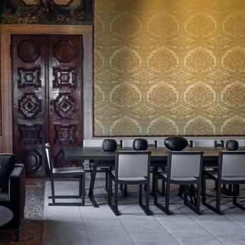 Salle à manger avec murs aux motifs géométriques dorés, portes ornementales et chaises noires à Aman Venice.