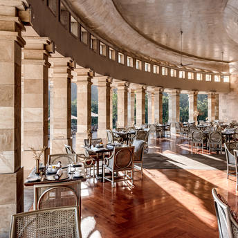 Curved colonnade dining venue at Amanjiwo with stone columns, wooden floors and natural light from arched windows.