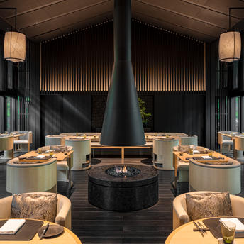 Dining pavilion at Aman Kyoto resort with central fireplace and symmetrical seating arrangement.