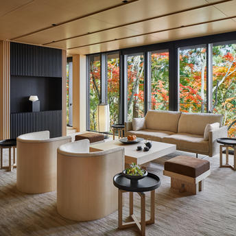Serene interior lounge at Aman Kyoto resort with curved wooden furniture, expansive windows framing autumn garden views, and minimalist décor.