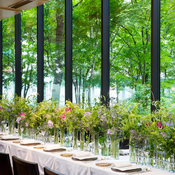 Café at Aman Tokyo with dining table overlooking verdant gardens through floor-to-ceiling windows.