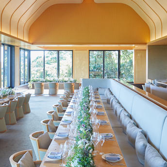 アマネムのリゾートで、アーチ型の天井と大きな窓のあるダイニングルーム。長いテーブルが緑の装飾で設えられている。