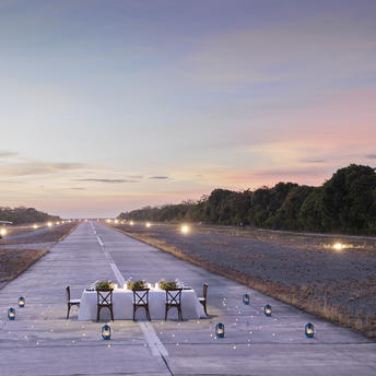 Amanpulo resort runway lit by evening lights, with silhouetted palm trees at dusk in the Philippines.