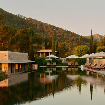 Amanruya's main pool at sunset, reflecting golden light on calm water with forested hillside beyond.