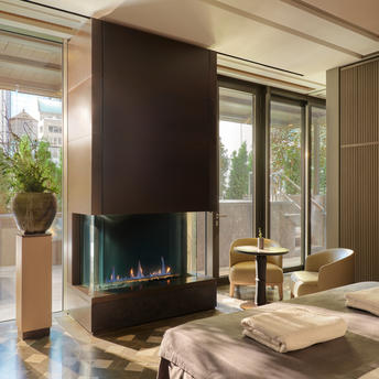 Spa lounge at Aman New York hotel with modern fireplace, floor-to-ceiling windows, and serene neutral tones.