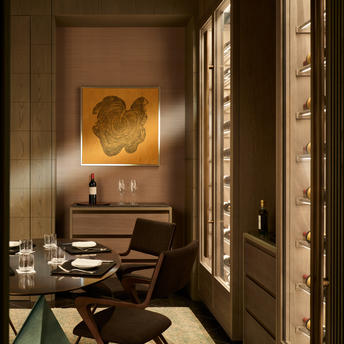 Biblioteca de vinos de Aman New York con estantes iluminados y obra de arte dorada en la pared.