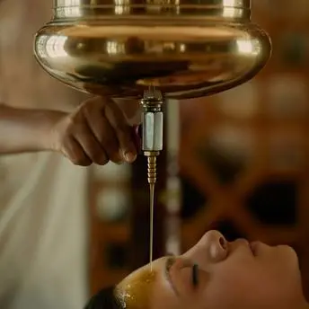 Wellness treatment at Amanbagh with therapist pouring warm oil over guest's face.