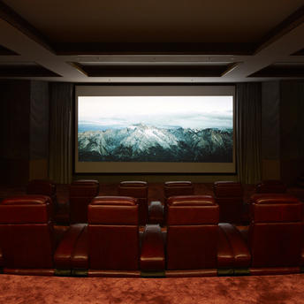 Cinema hall at Amandayan with red velvet seats facing a large screen displaying mountain landscape.