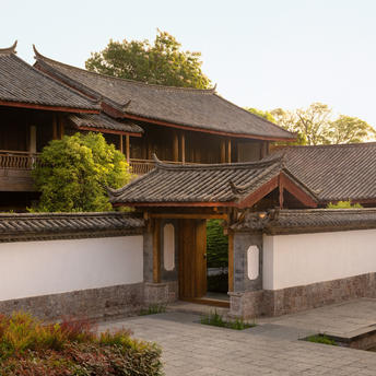 大研安缦度假村的传统中式庭院入口，白墙配黑瓦屋顶，晨光洒落。
