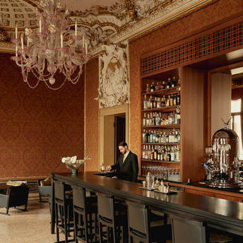 Bar at Aman Venice with crystal chandelier, wooden panelling and backlit spirits shelves.