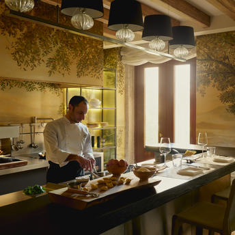 Cucina Palazzo presso Aman Venice, chef che prepara un piatto in una cucina con pareti dorate e travi a vista.