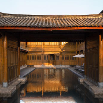 大研安缦度假村的游泳池在傍晚时分，传统建筑倒映在平静水面上。
