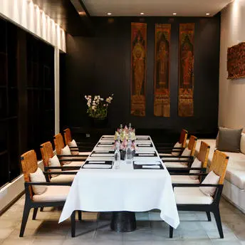 Formal dining room at Amansara with long white-clothed table, wooden chairs, and gold-toned artwork on dark walls.