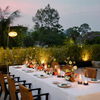 Outdoor dining celebration at Amansara with candlelit table set amongst tropical gardens at dusk.