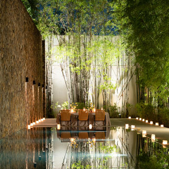 Candlelit celebration setup at Amansara with reflective water feature, wooden furnishings, and birch trees.