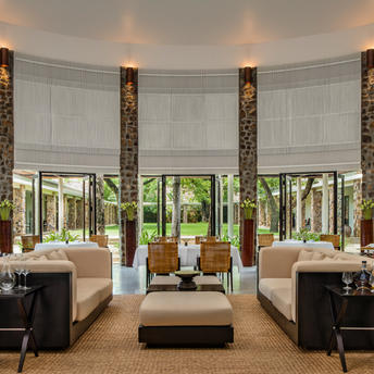Amansara dining room with symmetrical seating areas, stone columns, and garden views through large windows.