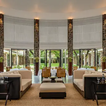 Amansara dining room with symmetrical seating areas, stone columns, and garden views through large windows.