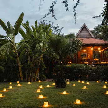Candlelit garden at Amansara with traditional Khmer architecture illuminated among tropical palms at dusk.