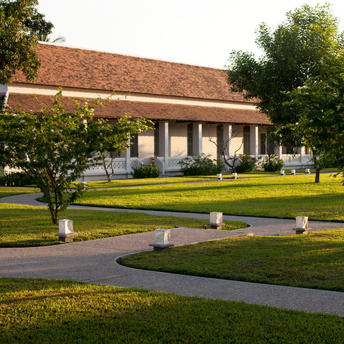 Manicured lawn at Amantaka with curved pathway, mature trees, and colonial-style building beyond.