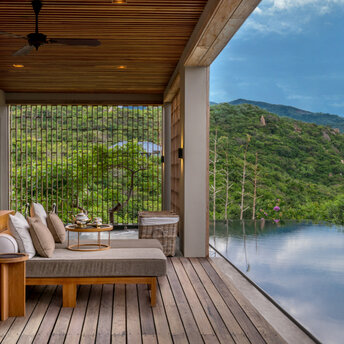 Wellness villa terrace at Amanoi with wooden deck, seating area and views over water towards forested hillside.