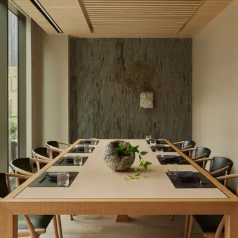 Salle de réunion privée à Aman New York avec table en bois clair et chaises noires.