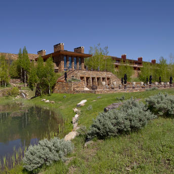 Amangani's north lawn sloping down to a pond, with the main building visible beyond manicured gardens and native vegetation.