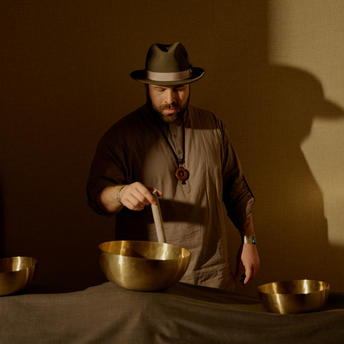 Person performing a sound bath meditation ritual at Aman New York, surrounded by brass singing bowls.