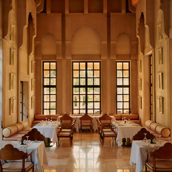 Warm-toned dining venue at Amanbagh with symmetrical arched alcoves, tall windows, and traditionally styled seating arrangements.
