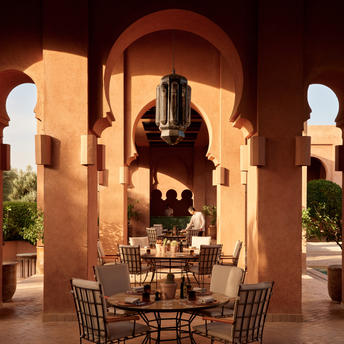 Pool terrace at Amanjena with dining setup beneath Moroccan archways at dusk.