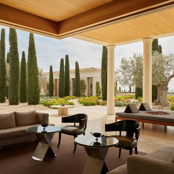 Bar seating area at Amanzoe with cypress trees visible through open columns, featuring modern furniture and terracotta tones.