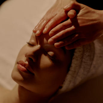 Therapist's hands gently massaging a guest's face during a facial treatment at Aman New York.