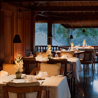 Amandari의 레스토랑에서 저녁 식사를 위해 세팅된 테이블들, 창문을 통해 발리의 풍경이 보이는 리조트 다이닝 공간.