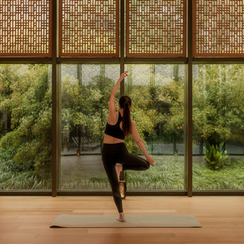 A woman practises yoga in the pilates and yoga studio at Amanyangyun Shanghai, with verdant garden views through floor-to-ceiling windows.