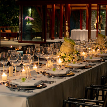 Candlelit dining table set for an evening event at Amanpuri, with warm amber lighting and seated guests in the background.