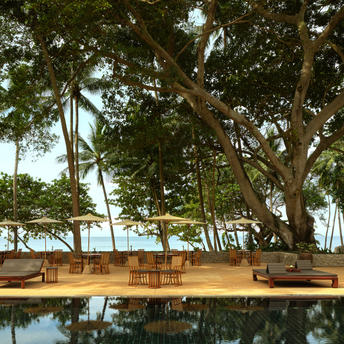 Wooden dining table set on a terrace at Amanpuri with views of the Andaman Sea and mature trees.