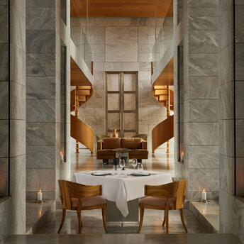 Private dining room at Amanzoe with marble columns, wooden chairs, and a central table set for two.