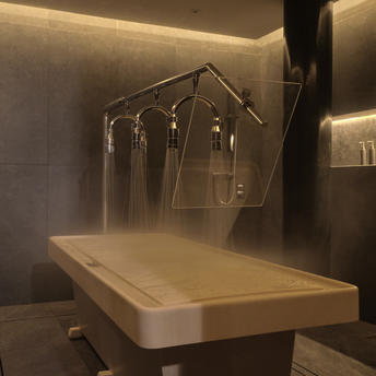 Spa treatment room at Amanpuri resort with a massage table and hanging wellness accessories beneath warm overhead lighting.