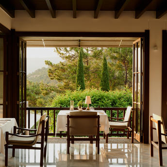 Private dining room at Amanruya with open doors framing a view of Turkish countryside and cypress trees.