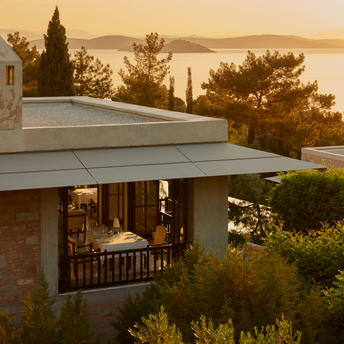 Amanruya restaurant terrace overlooking the sea at sunset, with warm golden light illuminating the dining area and coastal landscape beyond.