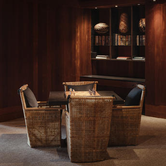 Takoda room at Amangani with woven chairs arranged around a marble table, warm wood panelling and display cabinet.