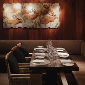 Amangani restaurant dining room with a long table set for service, warm lighting, and abstract artwork on the wall.