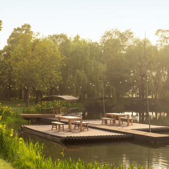 Bamboo rafts moored on a tranquil canal at Amanyangyun, surrounded by tall trees in golden morning light.