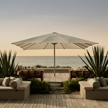 アマンヤラ リゾートの屋外リビングエリア。大型パラソルの下、デッキチェアとクッション付きシートが配置され、海の眺めを望む。