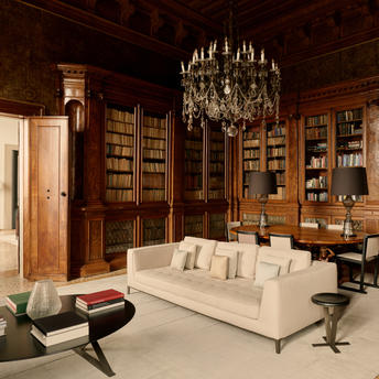 Bibliothèque élégante à Aman Venice avec canapé crème, lustres en cristal et boiseries anciennes.