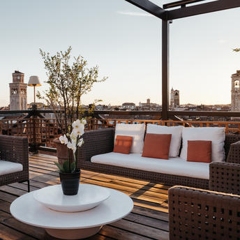 Terrasse sur le toit d'Aman Venice avec canapé, coussins orange et vue sur les toits de Venise.