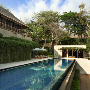 Swimming pool at Aman Villas at Nusa Dua, with tropical trees and villa architecture visible beyond.